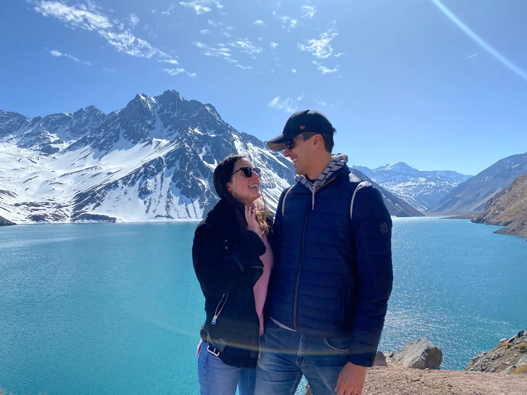 Vale y Fede sonriéndose frente a un lago turquesa y la cordillera nevada.
